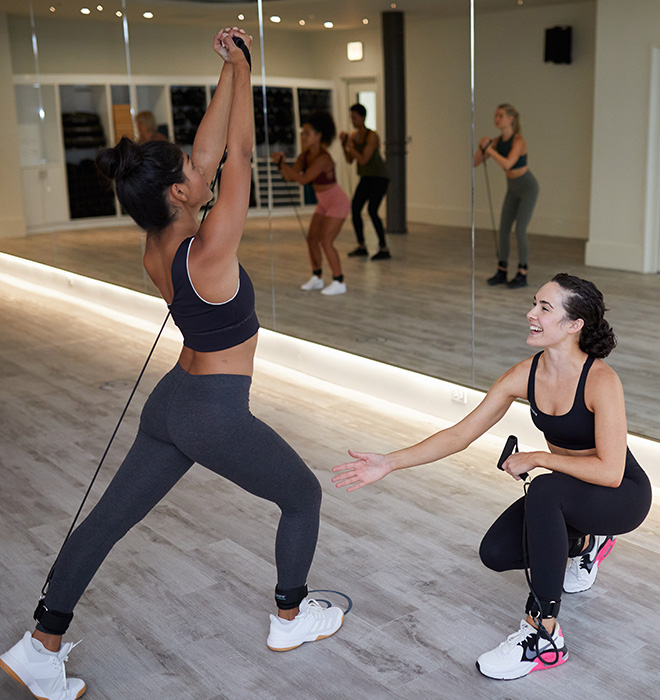 Smiling P.volve trainer encourages a member while she performs an exercise